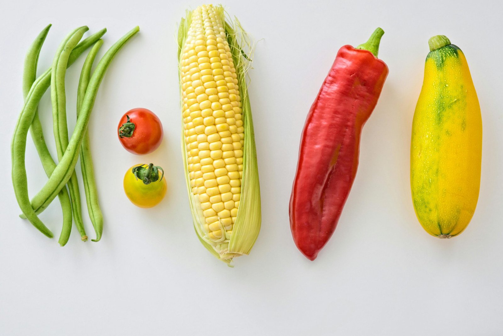 A vibrant assortment of fresh vegetables including corn, peppers, beans, and tomatoes.