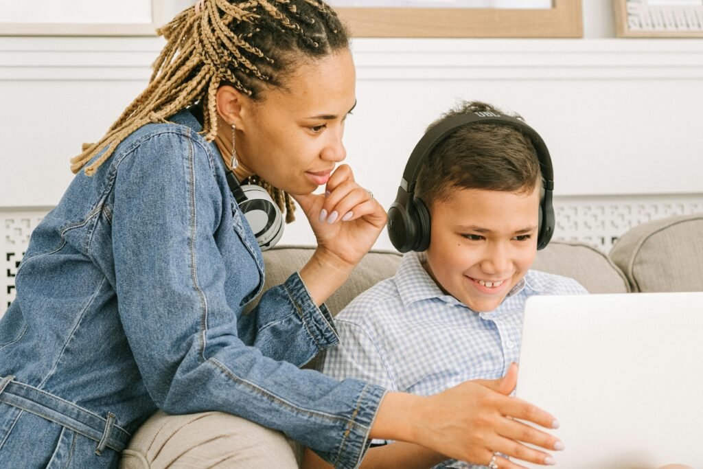 A mother and her son share a joyful online learning experience at home, smiling and engaged.